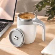 Pearl white self-stirring mug with coffee on a desk next to a laptop